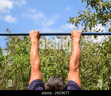 Hands on the bar close-up. The man pulls himself up on the bar. Playing sports in the fresh air. Horizontal bar. Stock Photo