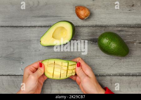 Tabletop view, young woman hands holding avocado with cuts, getting out the pulp. Stock Photo