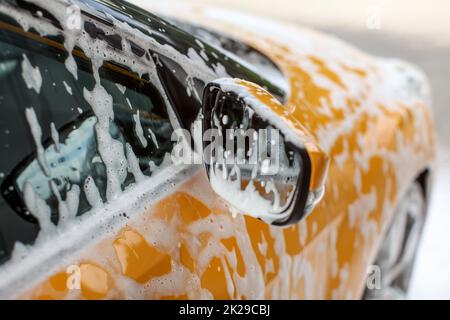 Detail on yellow car side mirror, covered with shampoo and foam spots, when washed in carwash. Stock Photo