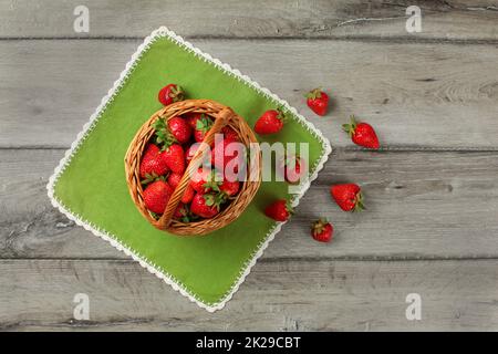 Tabletop view, small basket full of strawberries, some of them spilled on green table cloth under it. Stock Photo