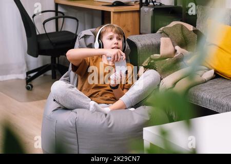 Boy teenager playing video game with joystick sitting on frameless beanbag chair Stock Photo