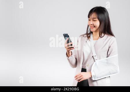 Woman confident smiling broken arm after accident and wear arm splint for treatment and hold smartphone Stock Photo