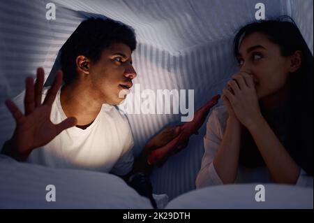 Husband telling wife scary story for under blanket Stock Photo