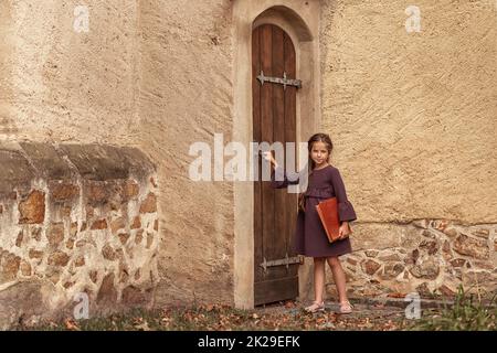 Portrait of a beautiful little girl with an old encyclopedia in her hands in the courtyard of the house. Stock Photo