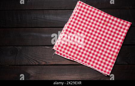 folded red and white cotton kitchen napkin on a wooden brown background, top view, copy space Stock Photo