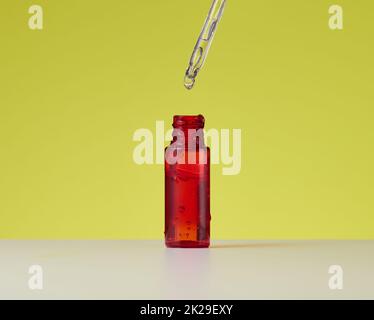 essential oil falling from the amber glass dropper. Red bottle of cosmetic oil with a pipette Stock Photo