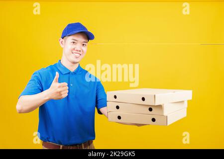 delivery service man standing he smile wearing blue t-shirt uniform hold give food order pizza cardboard boxes and show thumb up Stock Photo