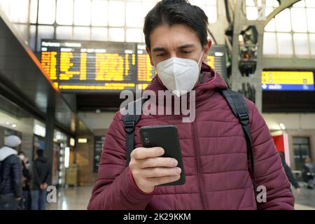 Traveler man wearing KN95 FFP2 protective face mask at the airport. Young caucasian man with behind timetables board of departures arrivals checking online ticket of his flight. Stock Photo