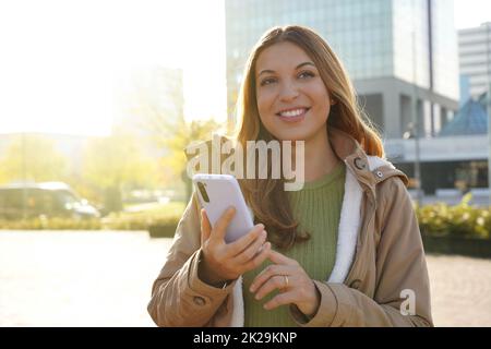 Smiling beautiful girl holding smartphone outside on sunset Stock Photo