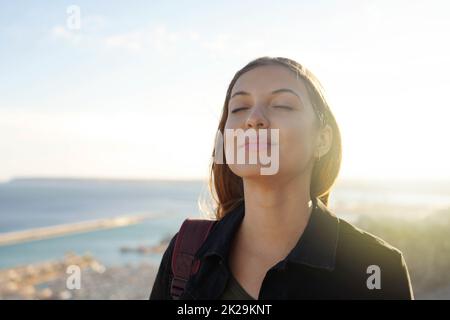 Beautiful young woman with closed eyes breathing relaxing enjoying sun at sunset. Beauty sunshine girl portrait. Stock Photo