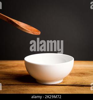 A white ceramic cup, a wooden spoon above it on a wooden table. Stock Photo