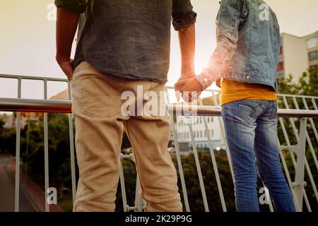 Taking in the sunset together. Rearview shot of a couple standing together on a city bridge and looking at the view. Stock Photo