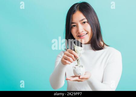 woman holding piggy bank on hands and putting dollars money banknotes Stock Photo