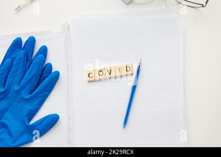 The inscription covid on a medical background, next to gloves, a pen, glasses and papers with patient data. Medical theme. Concept: vaccination against coronavirus. Stock Photo