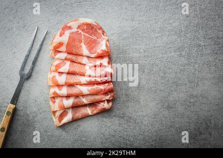 Italian dried ham. Coppa Stagionata with fork on kitchen table. Stock Photo