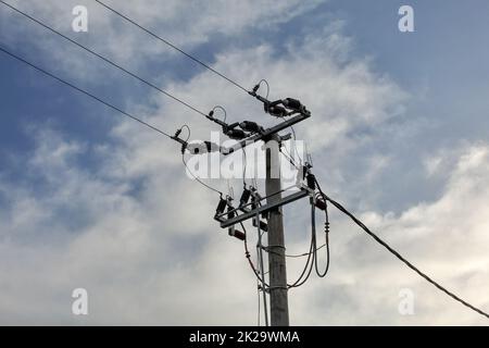 Small concrete pillar with power lines, sky with clouds in background. Stock Photo