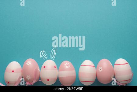 Pink Easter eggs in a row on blue, one with bunny ears Stock Photo