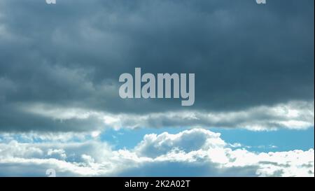 Blue sky with thunderclouds. The sun breaks through the clouds. Black clouds. Banner. Stock Photo
