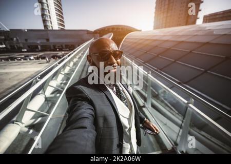 A handsome mature bearded bald dapper black guy is taking a first-person selfie on the street; an elegant African businessman in a suit is shooting hi Stock Photo
