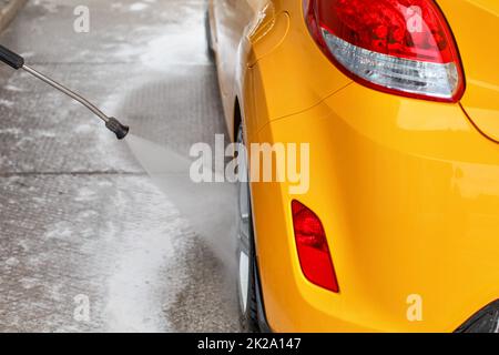 Rear wheel of yellow car washed with jet water in self serve carwash. View from behind. Stock Photo