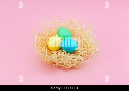 Easter eggs painted in pastel colors in hay nest against a pink background. Stock Photo