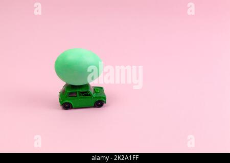 Toy green car with Easter egg on the roof. Easter card with space for text on a pink background. Stock Photo