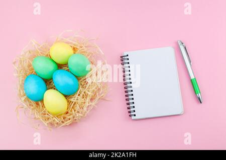 Blank notepad and pen on trendy dark pink background. Easter eggs painted in pastel colors in hay nest against a pink background. Stock Photo