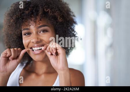 Getting those hard to reach places. Shot of a young woman flossing her teeth in the mirror. Stock Photo