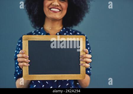 Put you message on my chalkboard. Studio shot of a young woman holding a blank chalkboard against a gray background. Stock Photo