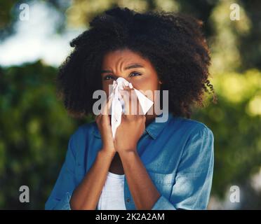 Its allergy season.... Portrait of a young woman blowing her nose with a tissue outside. Stock Photo