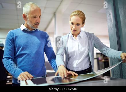 Assuring quality throughout the process. Two publishers assessing the quality of printed work in a factory. Stock Photo