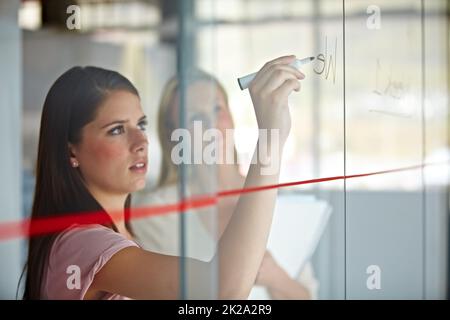 Charting the expected results. A young businesswoman writing down plans on a glass pane. Stock Photo