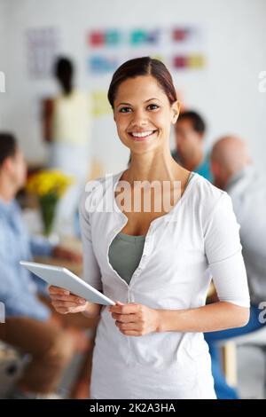 All your designing needs in her hands. Portrait of a young professional working on a digital tablet with her coworkers sitting in the background. Stock Photo