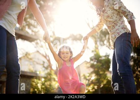 Having so much fun with her family. A cute little girl being swung by her mother and grandmother in the garden. Stock Photo