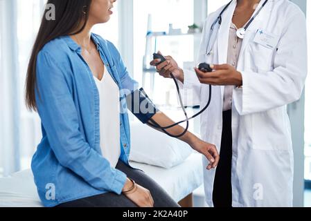Blood pressure tells a lot about your health. Shot of a young woman getting her blood pressure measured during a checkup with a doctor. Stock Photo