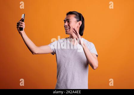 Smiling young man chatting on smartphone video conference. Remote communication, talking on teleconference, online meeting on mobile phone, teenager greeting interlocutor on videocall Stock Photo