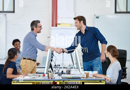 Another job well done. two designers shaking hands over their computers in an office. Stock Photo