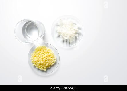 Crystal clear liquid in beaker, Flake salt and Candelilla Wax in Chemical Watch Glass. Chemicals ingredients on laboratory table. Top View Stock Photo
