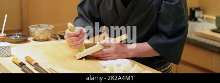 Chef grinding fresh wasabi on a wooden grater. Stock Photo