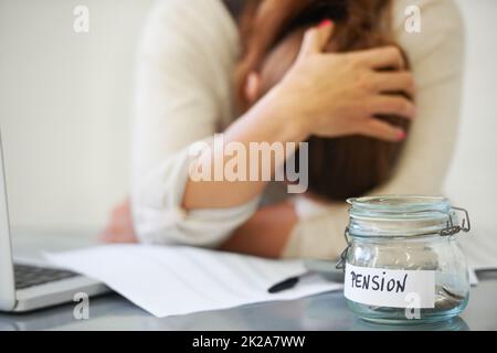 All work and no pay. An upset woman holding her head with a jar of pennies on her desk. Stock Photo