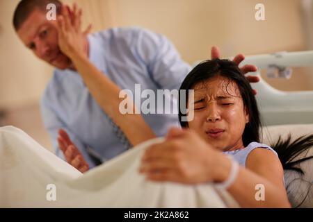 Youre not helping.... Shot of a young woman giving birth with her husband supporting her in the background. Stock Photo