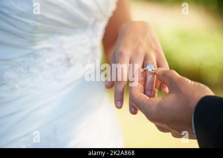 The symbol of their commitment. Closeup of a groom putting the ring on his brides finger on their wedding day. Stock Photo