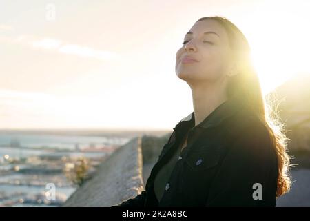 Pretty young woman with closed eyes breathing relaxing enjoying sun at sunset. Beauty sunshine girl side profile portrait. Positive emotion life success mind peace concept. Stock Photo