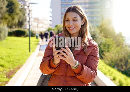 Young woman outdoor using smartphone wearing winter coat watching video streaming Stock Photo