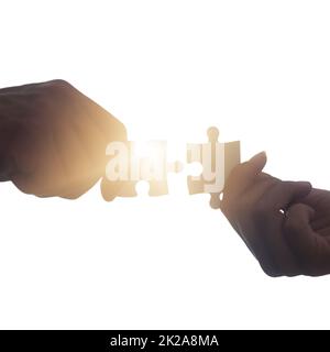 Problems can be solved quicker together. Closeup shot of two unrecognisable people putting two puzzle pieces together. Stock Photo