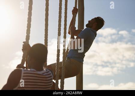 Mind over matter. Shot of two young men climbing up ropes at a military bootcamp. Stock Photo