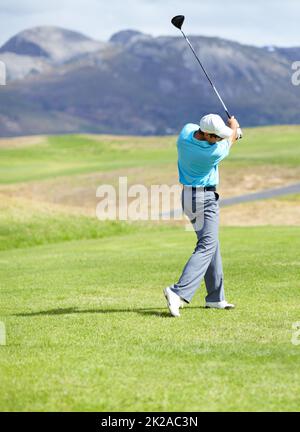 Driving it down the fairway. A young, fit male golfer following through after driving his ball down the fairway. Stock Photo