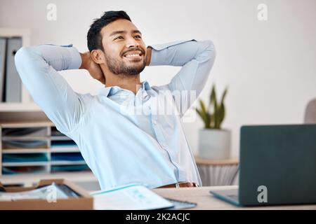 Businessman relaxing at a desk in the office at his corporate job after finishing a project. Happy, calm and stress free man employee sitting and Stock Photo