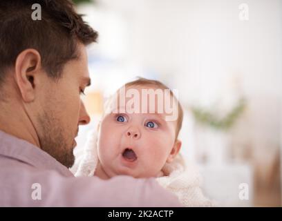 Hes an amazing father. A cute baby girl looking over her fathers shoulder as he holds her. Stock Photo