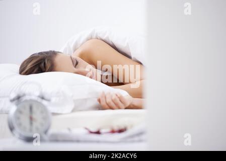 Getting her 8 hours. A woman sleeping in her bed with an alarm clock in the foreground. Stock Photo